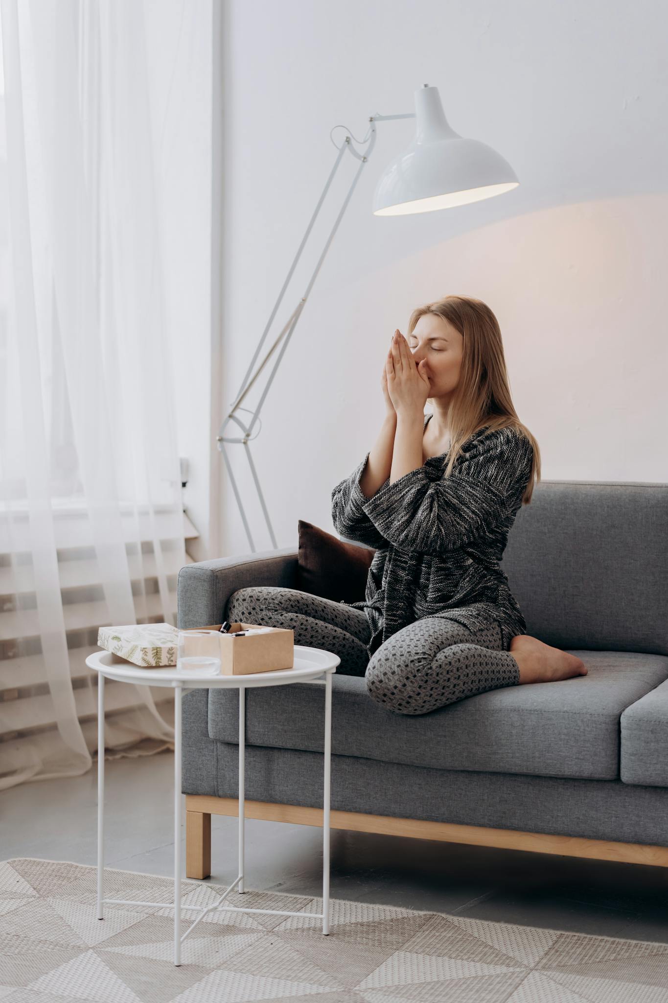 A woman sits cross-legged on a couch meditating in a serene indoor setting.